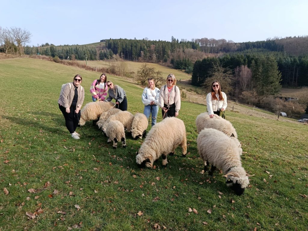 eine Gruppe junger Frauen stehen gemeinsam mit der Schafherde von Hof-Naturverbunden auf einer Wiese in der Natur im Sauerland